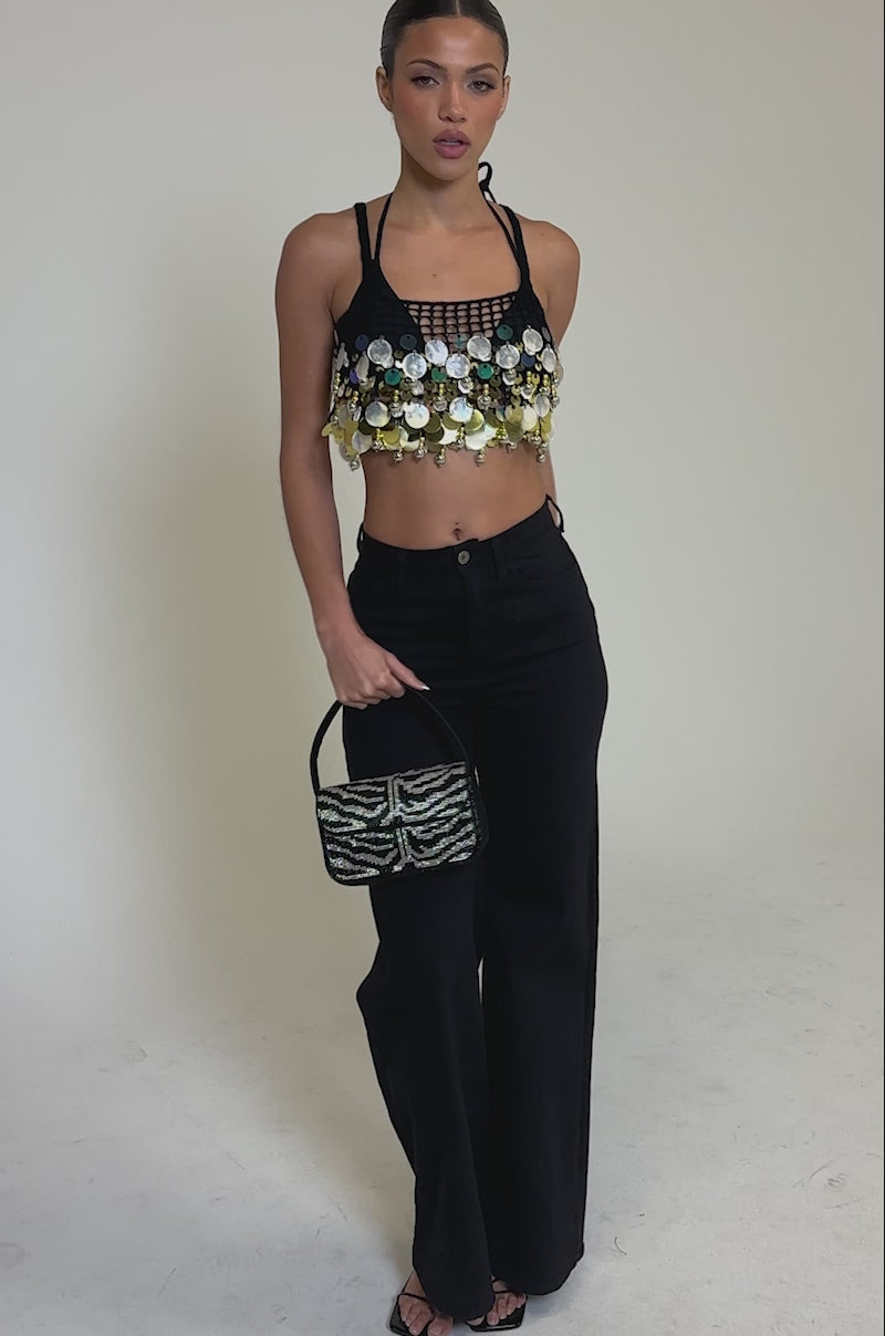 Video of woman modeling the RESORT LIVING SEQUIN CROCHET TOP with high-waisted black jeans, posing confidently against a neutral background—an ideal choice for a festival party look.