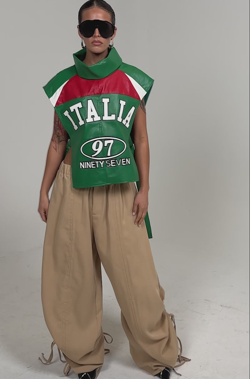 Video of woman modeling the CATCHING FLIGHTS EMBROIDERED VEST—an oversized green, red, and white sleeveless statement piece styled with wide-leg beige pants and sunglasses.