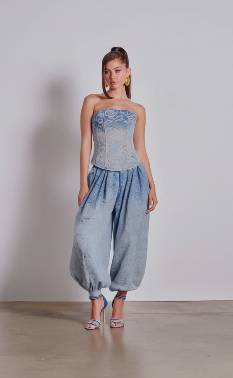 A video of a woman in the DENIM FOR DAYS ZIP UP CORSET, a chic blue denim strapless top, paired with matching relaxed pants and high-heeled sandals.