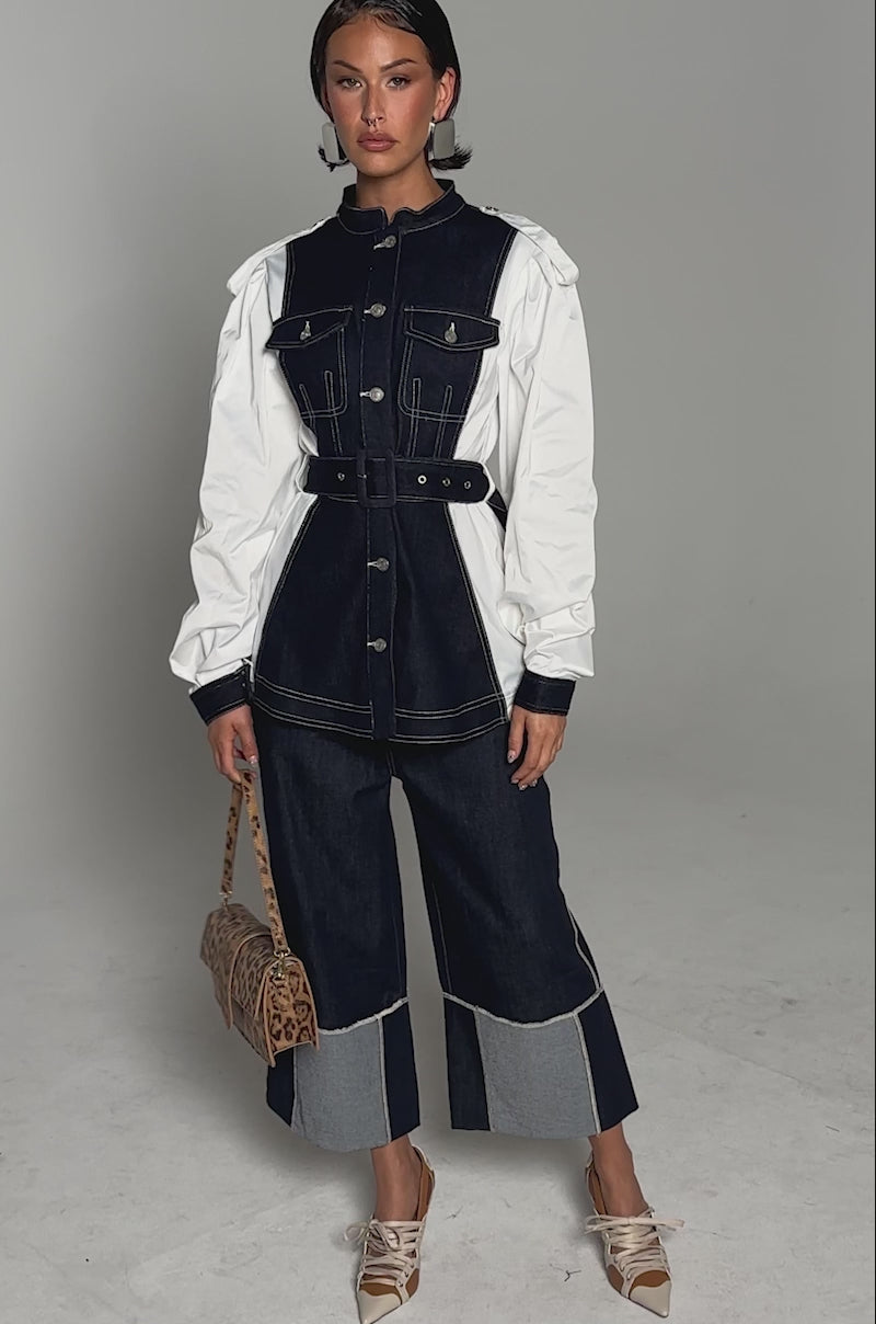 A video of a woman wearing the DIANA DENIM AND POPLIN BUTTON DOWN, styled with matching wide-leg denim pants, a leopard print handbag, and beige lace-up shoes against a plain light gray background.