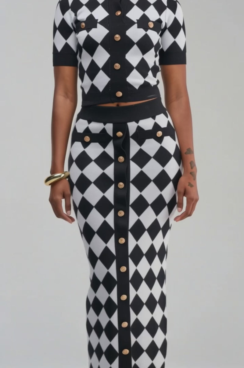 Video of a woman modeling the THE BEST PART BUTTON DOWN TOP—a black and white diamond-patterned argyle knit design with a cropped fit and gold buttons.