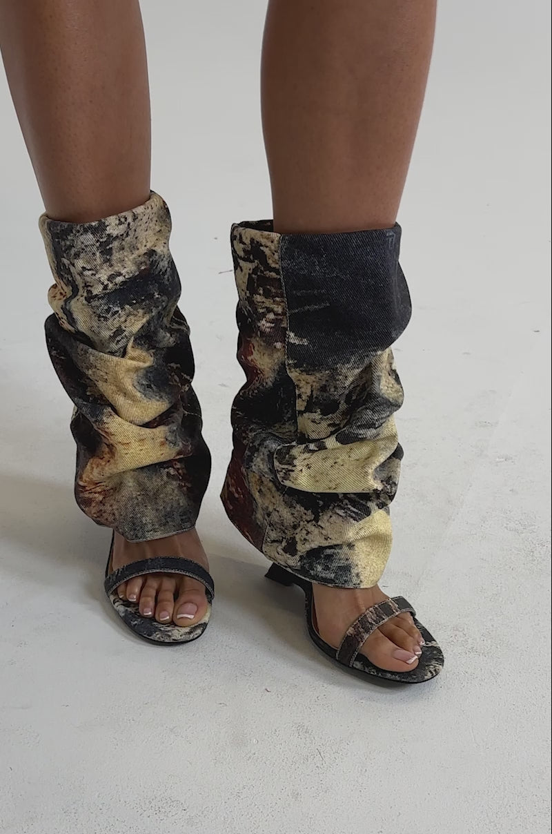 A video of a model wearing the AZALEA WANG RAXA MULTI OPEN TOE BOOTIE and slouchy leg warmers with an abstract yellow, black, and brown splatter paint pattern.