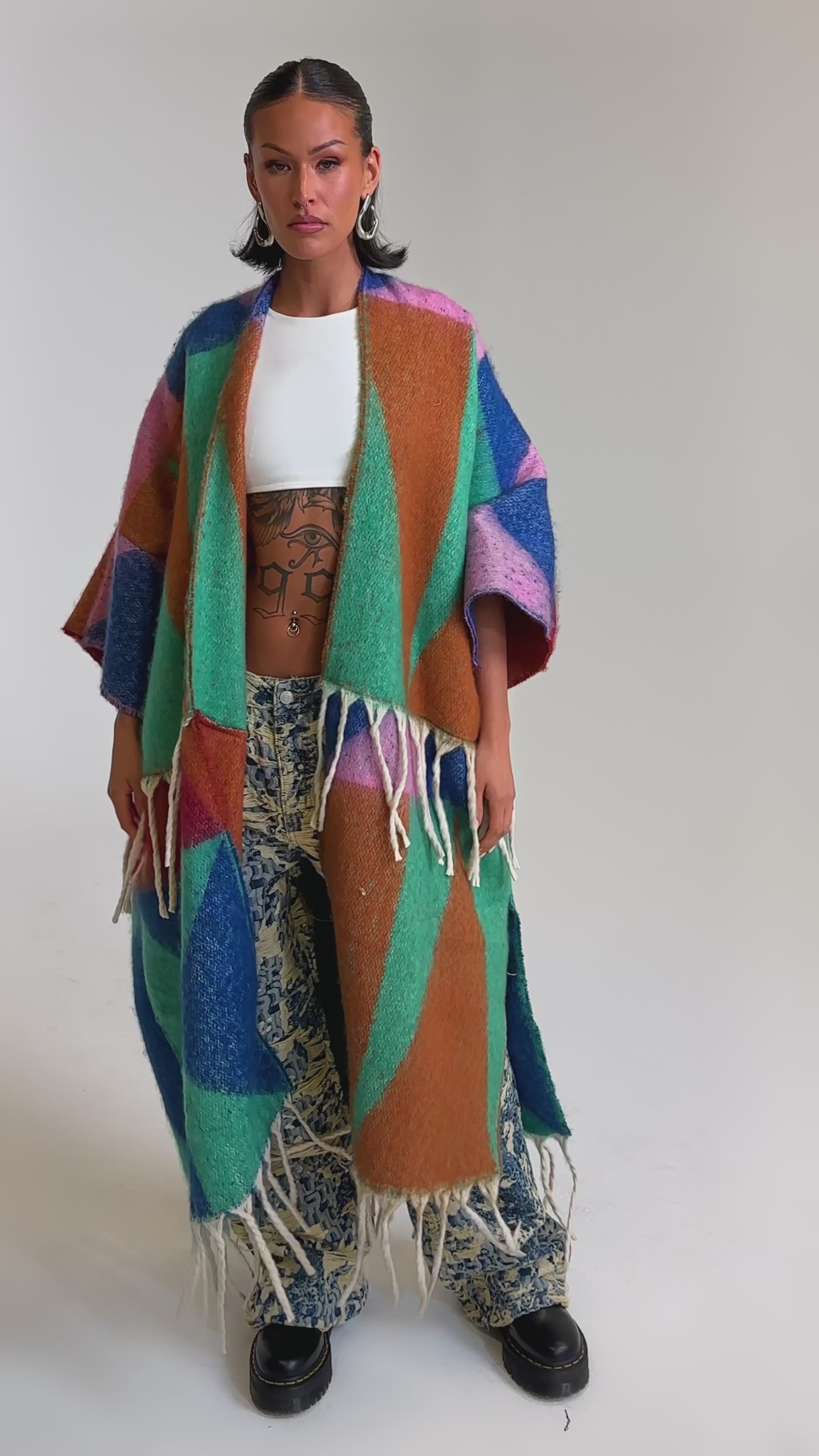 A video of a woman in the RENEWED DREAM TAPESTRY PANT—featuring a two-tone wide-leg silhouette with colorful geometric patterns and fringed detail.