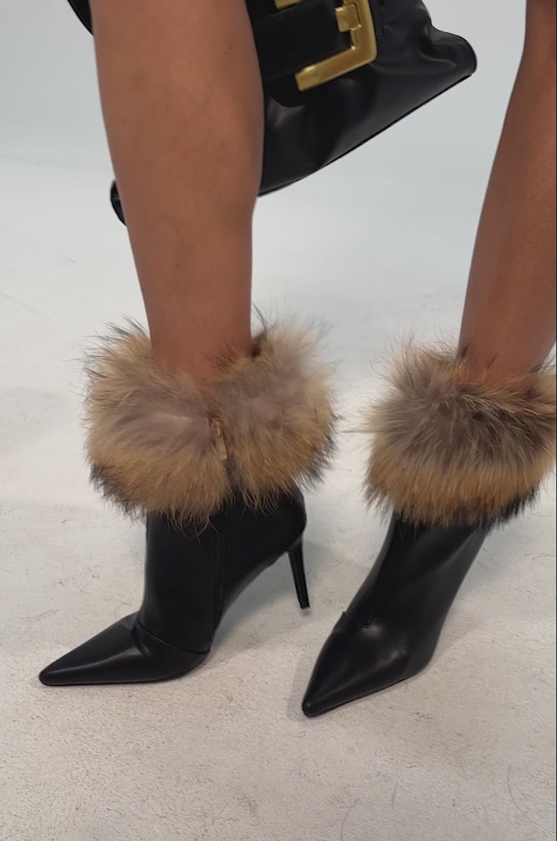 Video of woman modeling the AZALEA WANG BARLEY BLACK FUR CUFFED BOOTIE and holding a black handbag. The background is plain and light-colored.
