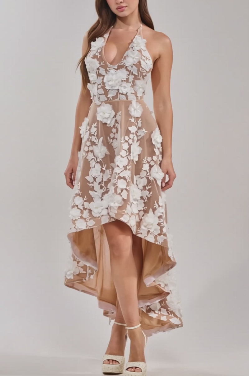 A video of a woman in the LILAH FLOWER APPLIQUE MIDI DRESS—a sleeveless, high-low nude dress with white floral embroidery—paired with platform heels.