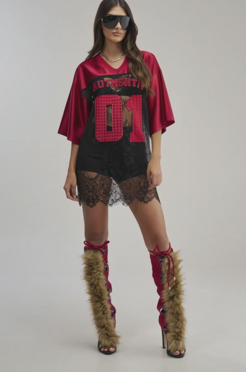 A video of a woman wearing large sunglasses, an IT GIRL LACE JERSEY DRESS with “AUTHENTIC 01,” and knee-high furry brown and red boots.