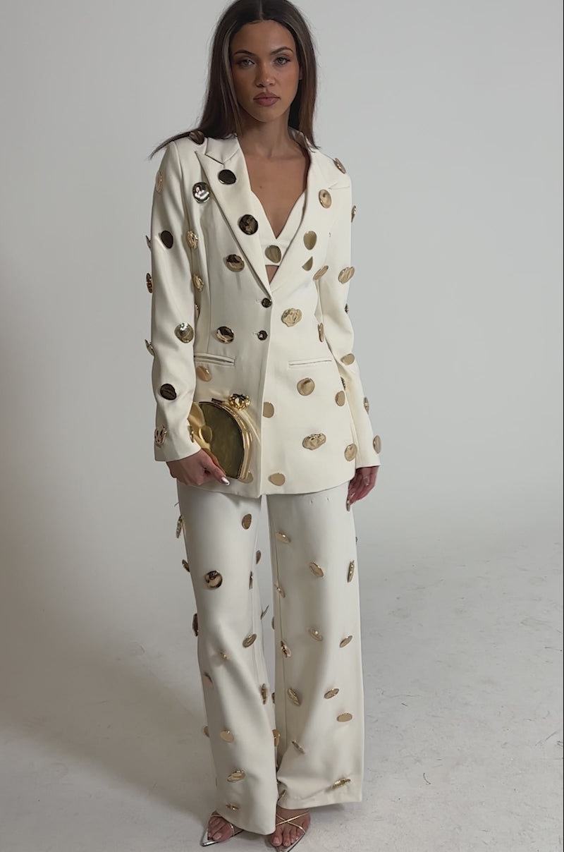 Video of woman modeling the SARASOTA EMBELLISHED BLAZER and holds a small gold clutch, standing against a plain light background.