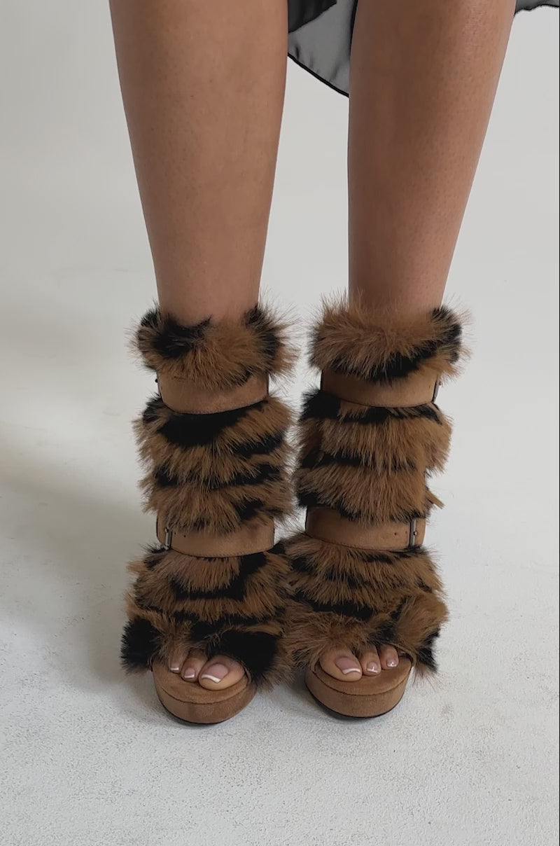 A video of a person wearing the AKIRA GOLD SERIOUS BROWN FUR BOOTIE—tan stilettos with multiple brown and black faux fur straps.