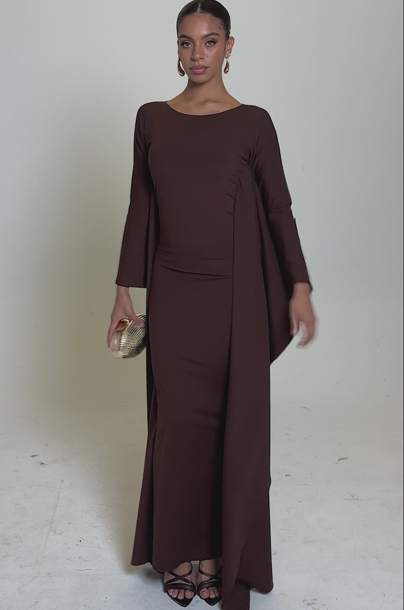 A video of a woman in the KYLIE MAXI DRESS WITH RUFFLE SLEEVES IN BROWN, styled with black heels and gold hoop earrings.
