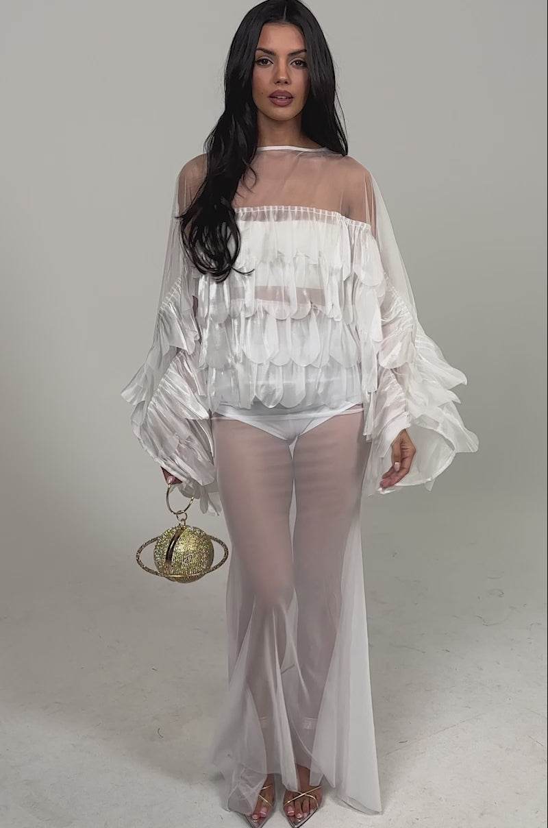 Video of woman modeling the RUFFLE CITY BLOUSE, an elegant long-sleeve top with ruffled, petal-like details, paired with matching sheer pants and holding a small gold bag against a plain white background.