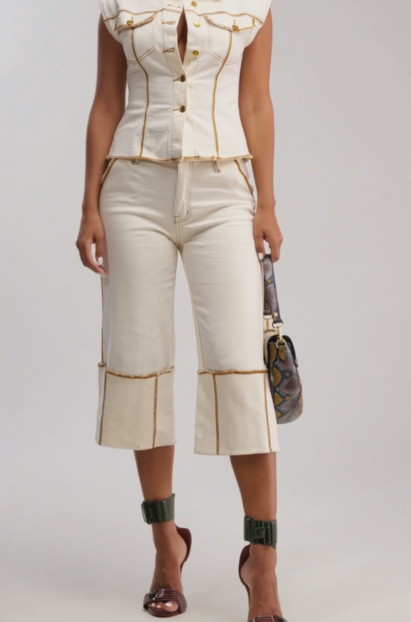 Video of woman modeling the IM ALL YOURS BUTTON DOWN, a sleeveless cream denim top styled utility-chic with matching high-waisted pants. She holds a snakeskin bag and gazes to the side against a plain background.