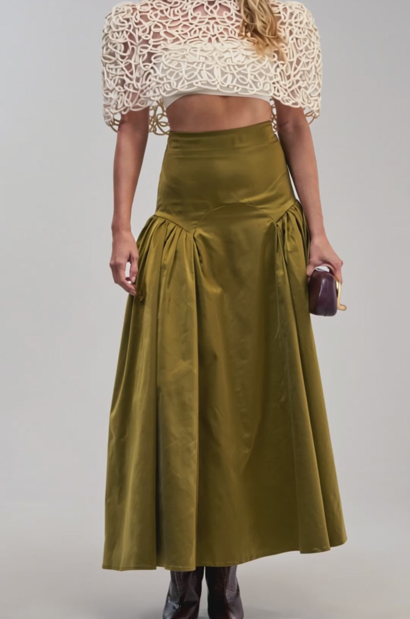 Video of a woman modeling the DANCING IN THE SUN MAXI SKIRT, showcasing its olive satin fabric and high-waisted, flared silhouette. 
