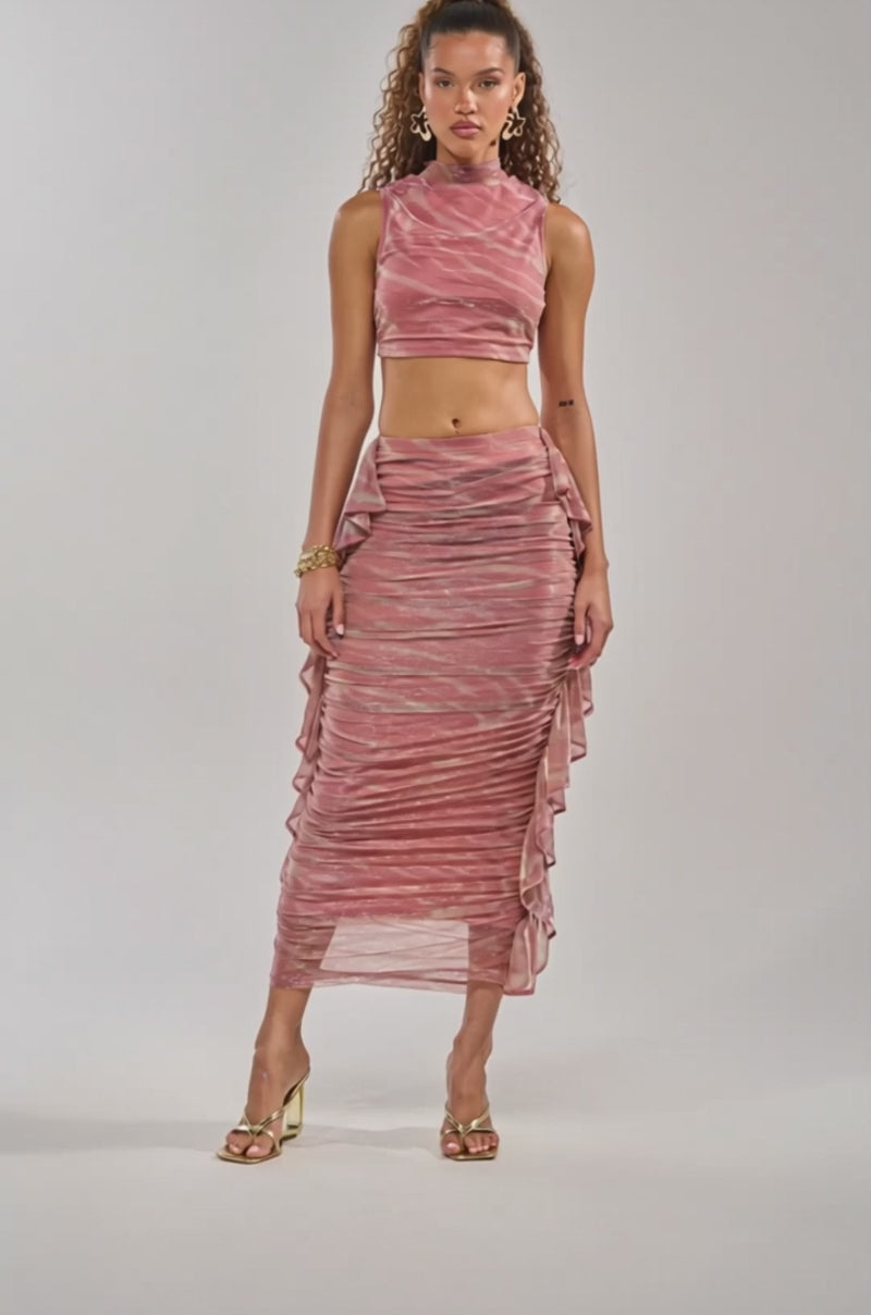 Video of woman modeling the PLAY WITH ME MOCK NECK TANK and matching skirt, accessorized with gold jewelry and sculptural earrings—perfect vacation wear against a neutral background.
