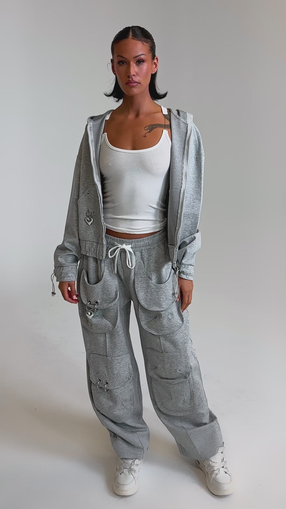 A video of a woman wearing the GET WITH IT WIDE LEG CARGO JOGGER, a light gray hooded jacket, white tank top, and white sneakers against a plain light background.