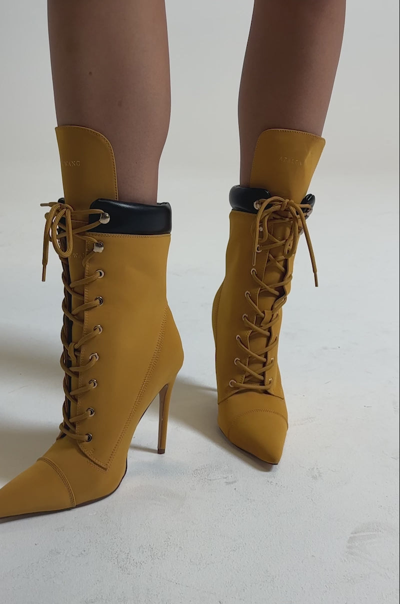 A video of a person on a neutral background wearing AZALEA WANG XIOMARAN YELLOW BOOTIE stiletto heel boots, featuring pointed toes and black collar details.