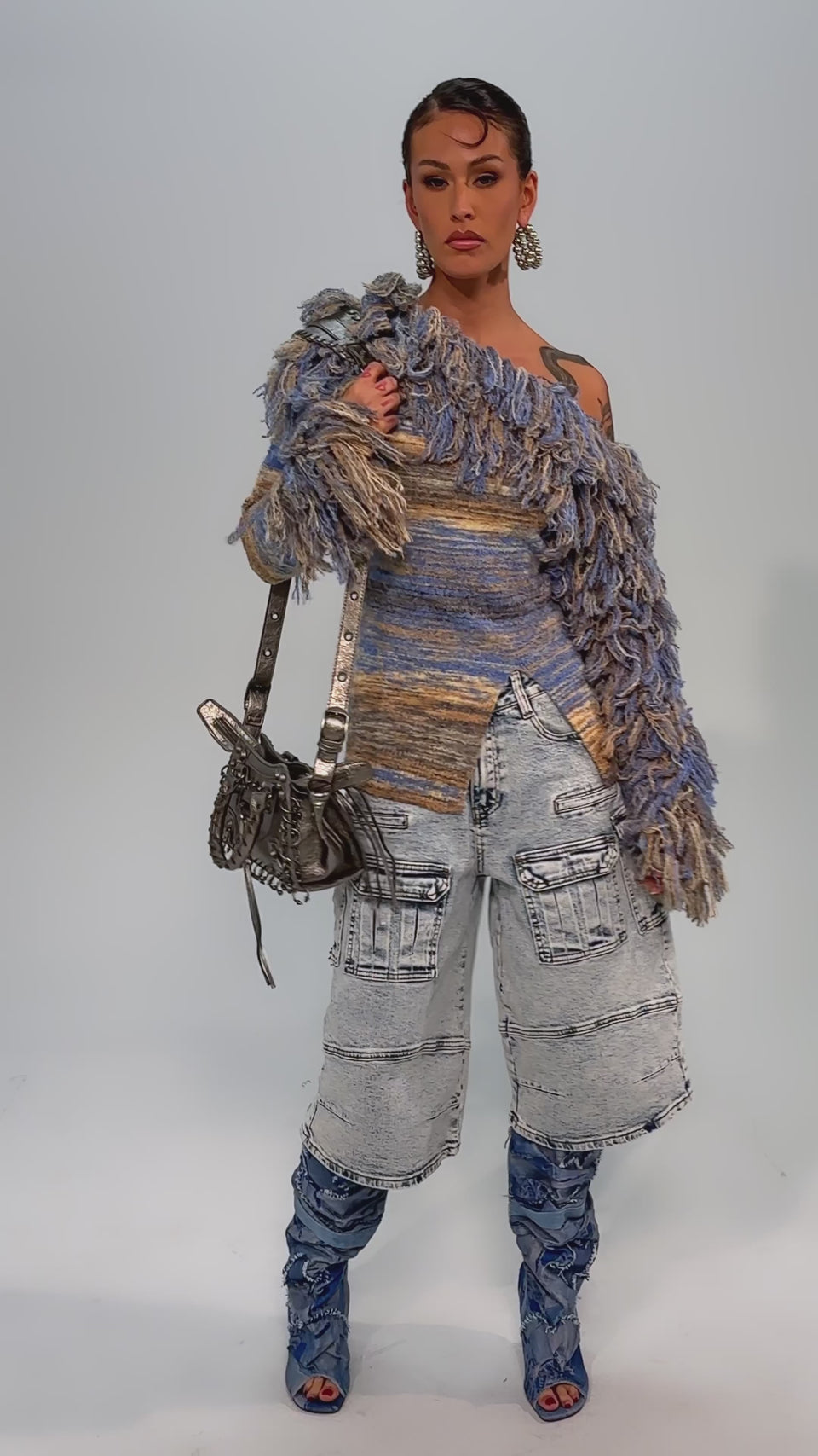 Video of woman modeling the FORGET ME NOT DENIM CARGO BERMUDA SHORT, paired with a multicolored textured sweater and blue knee-high boots against a plain gray background.