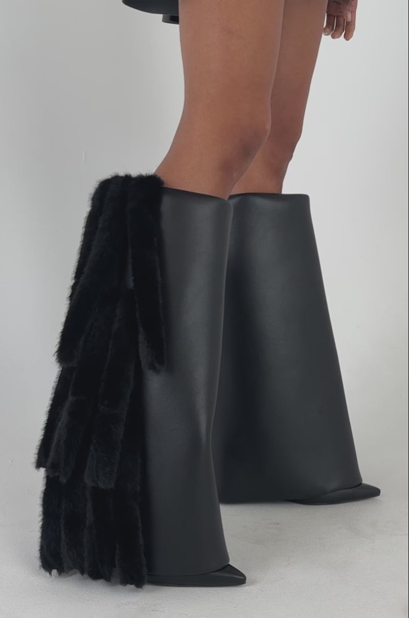 Video of a woman modeling the AKIRA GOLD KAIZEN BLACK FUR DETAIL BOOTS—one boot adorned with black faux fur strips—stands against a plain background.