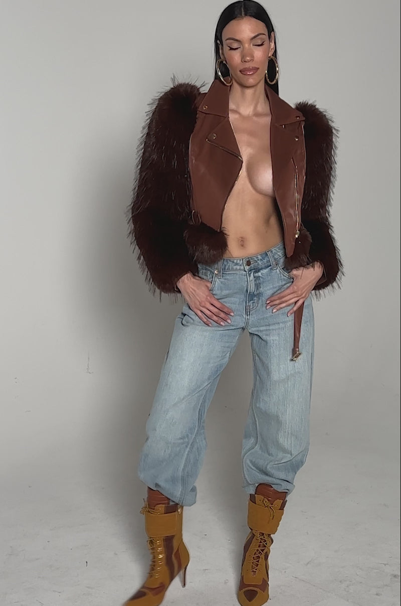 Video of woman modeling the SPEND IT ALL FUR TRIM MOTO— a brown faux leather moto jacket with faux fur sleeves—paired with light blue jeans. 