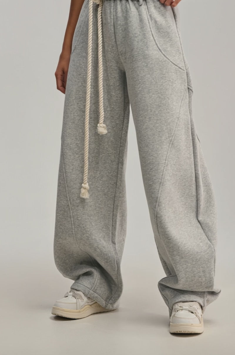 Video of woman modeling the IT GIRL WIDE LEG SWEATPANT in light gray, featuring a ruffled waistband and thick rope drawstring, paired with white sneakers. 