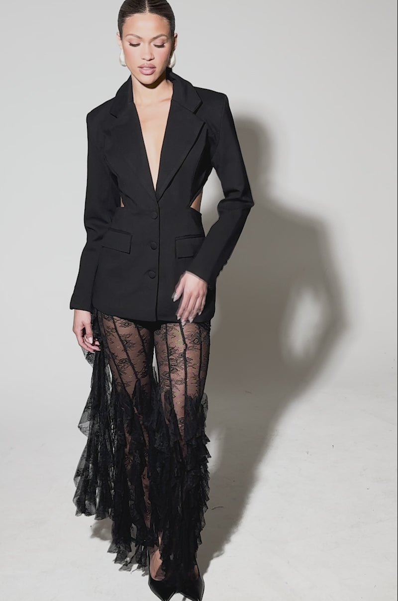Video of woman modeling the PARTY IN THE BACK CUTOUT BLAZER, styled with sheer black lace pants and ruffled lace details, plus black pointed-toe heels, set against a plain light gray background.