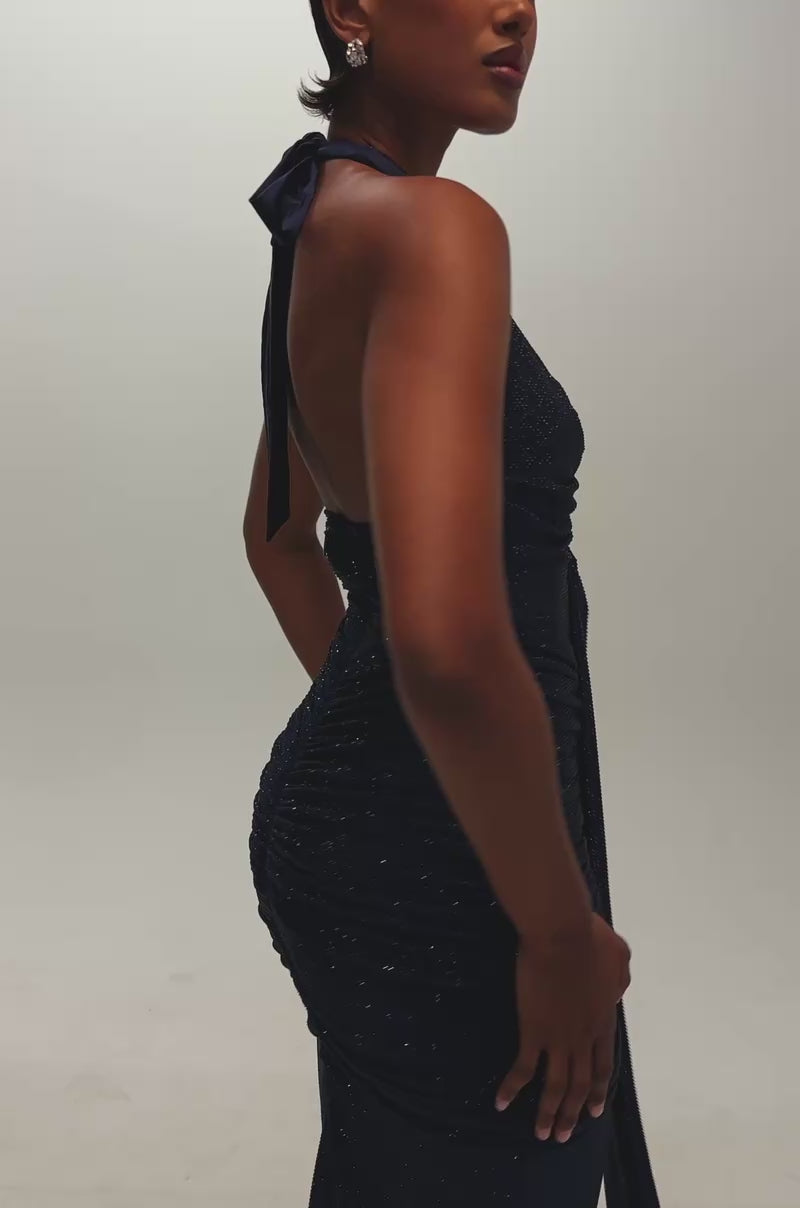 Video of a woman modeling the GOLDEN DUNES RHINESTONE MAXI DRESS—a deep blue, halter-neck, floor-length ruched maxi with a front drape.
