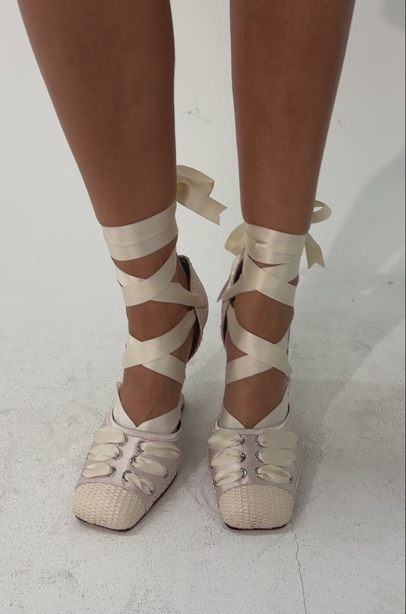 A video of a person wearing the AKIRA GOLD TENDU IVORY BALLET LACE UP NOVELTY HEEL PUMPS with ribbon ankle straps, set against a neutral background.