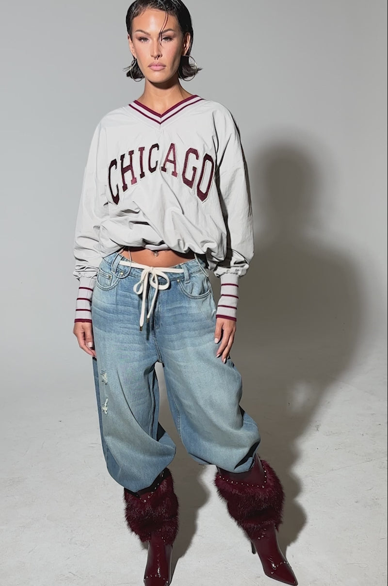 Video of woman modeling the CHICAGO V-NECK SWEATSHIRT, paired with baggy ripped jeans and maroon fur-trimmed pointed-heel boots, against a plain light background.