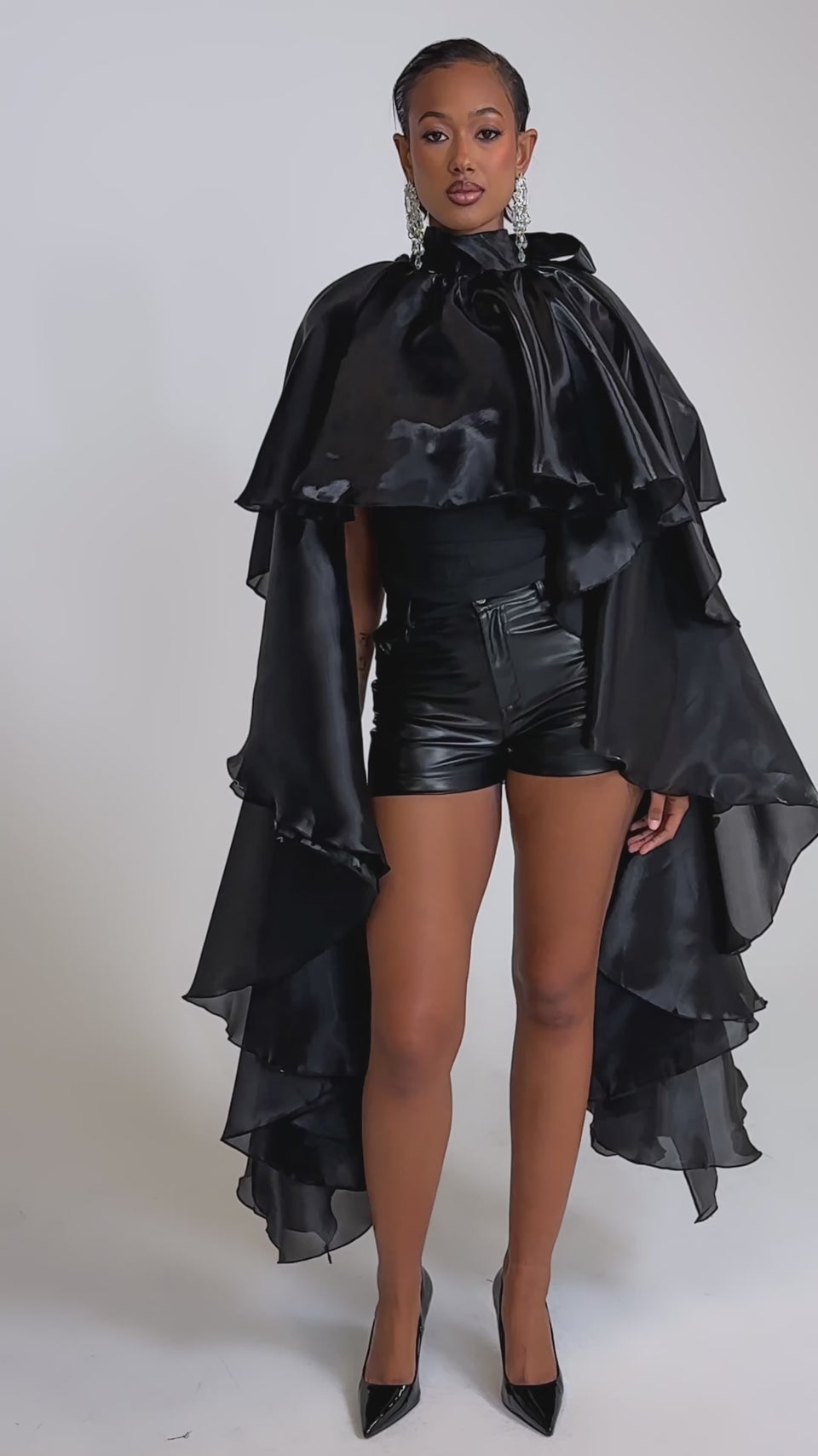 A video of a woman wearing the COOLEST ON THE BLOCK BLOUSE and leather shorts. Black heels and slicked-back hair complete her bold, modern look.