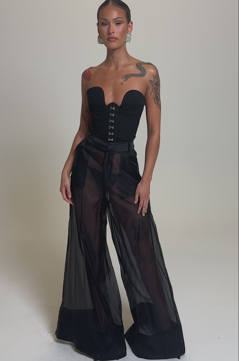 Video of woman modeling the LOUD AND LUX TROUSER, paired with a black strapless corset top. Her tattoos accent her arm and shoulder, and her hair is pulled back. The outfit stands out against a plain gray background.
