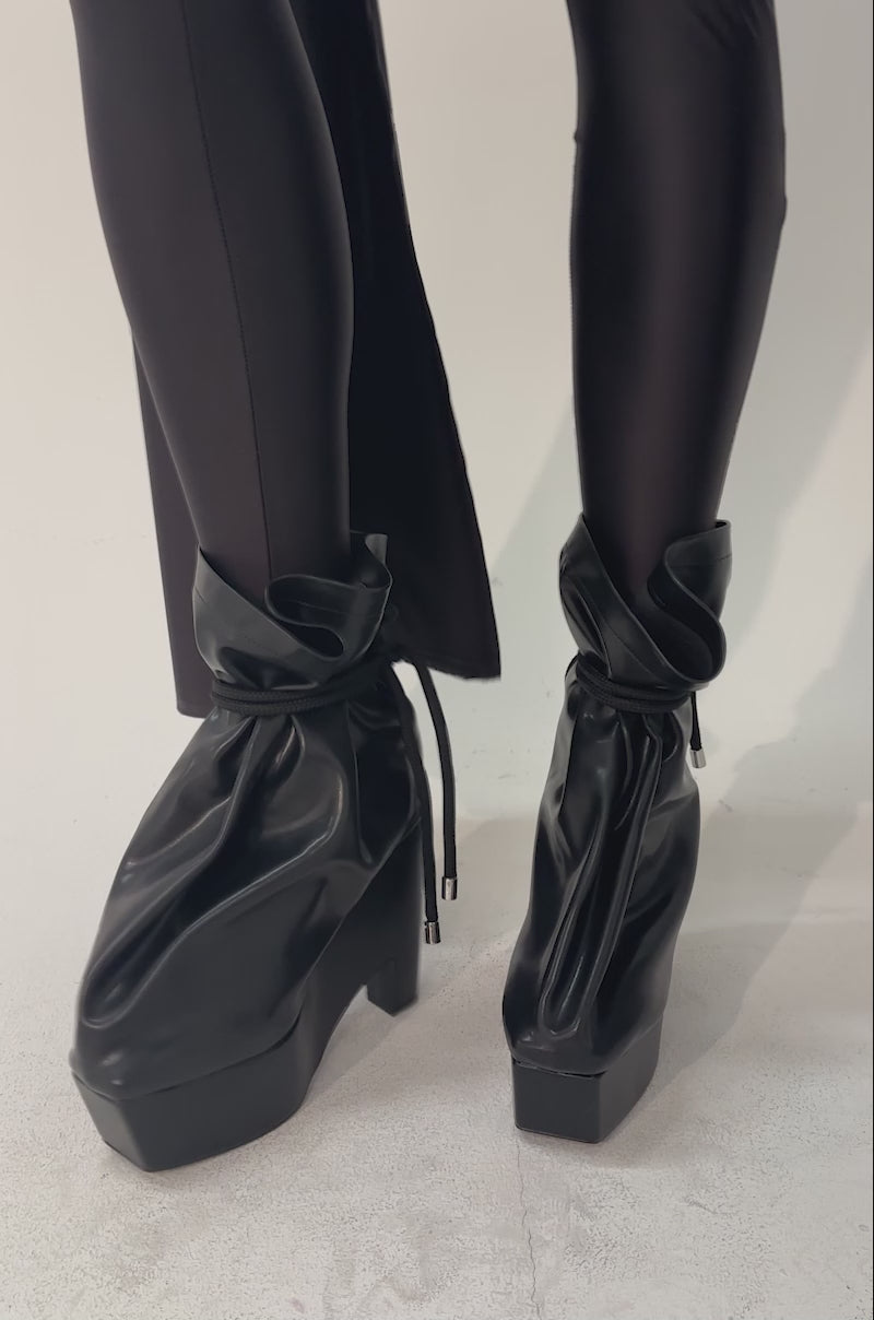 A video of a woman wearing shiny black leggings and the AKIRA GOLD EPIGRAM PU SLOUCH CHUNKY HEEL BOOTIE.
