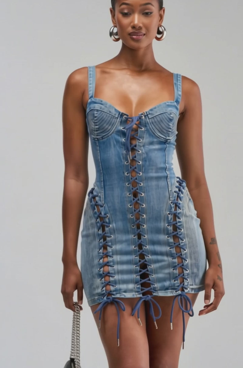 Video of a woman modeling the READY FOR THE RODEO LACE UP DENIM DRESS. This blue denim mini dress features bodycon fit with corset-style lacing down the front and sides, shoulder straps.