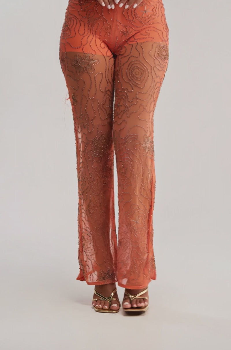 Video of woman modeling the KATE EMBELLISHED MESH PANT IN ORANGE, featuring sheer fabric and intricate beadwork, paired with gold high-heeled sandals.