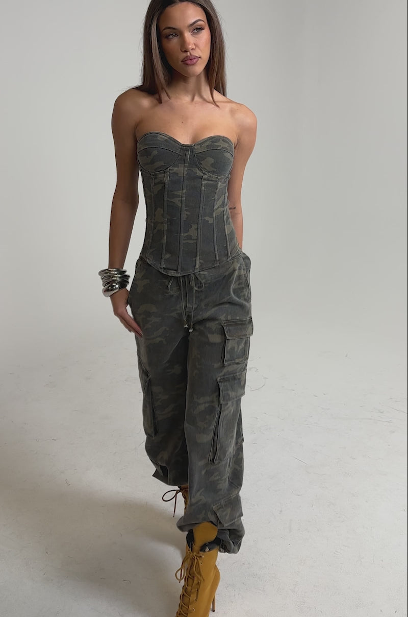 Video of woman modeling the Down and Dirty Cargo Pant featuring a wide-leg camo print, styled with a strapless fitted camouflage corset top, yellow lace-up boots, and silver bangles against a plain light background.