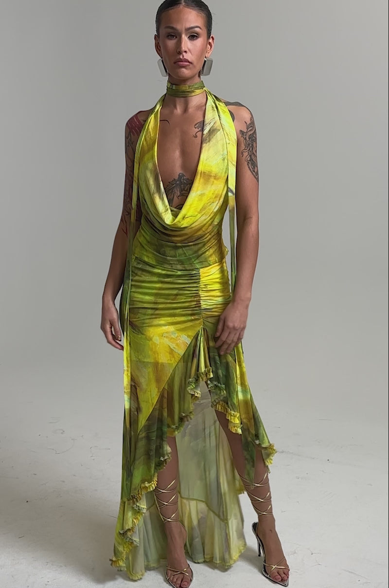 Video of woman modeling the TELL ME MORE COWL NECK BLOUSE, a yellow-green sleeveless top with a draped cowl neckline and large geometric earrings, standing against a plain light background.