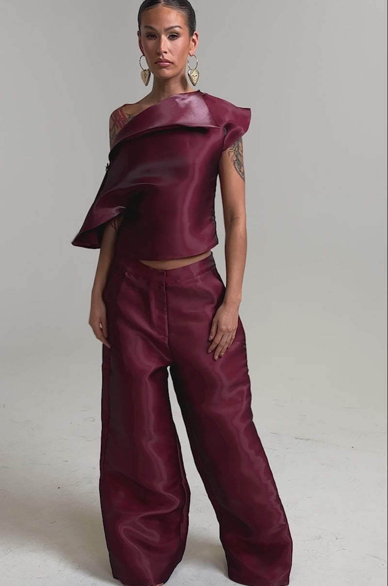 Video of woman modeling the ON FIRE TROUSER pants and a shiny, deep burgundy asymmetrical top with sculptural folds.