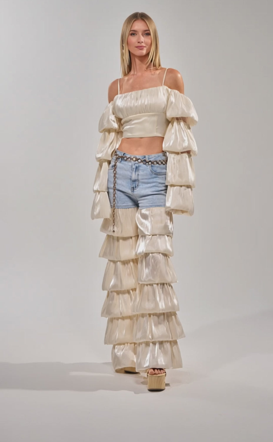 Video of woman modeling the BOUNCIN AROUND DENIM RUFFLE PANT paired with a cream off-shoulder ruffle top, styled with a chain belt over statement denim.