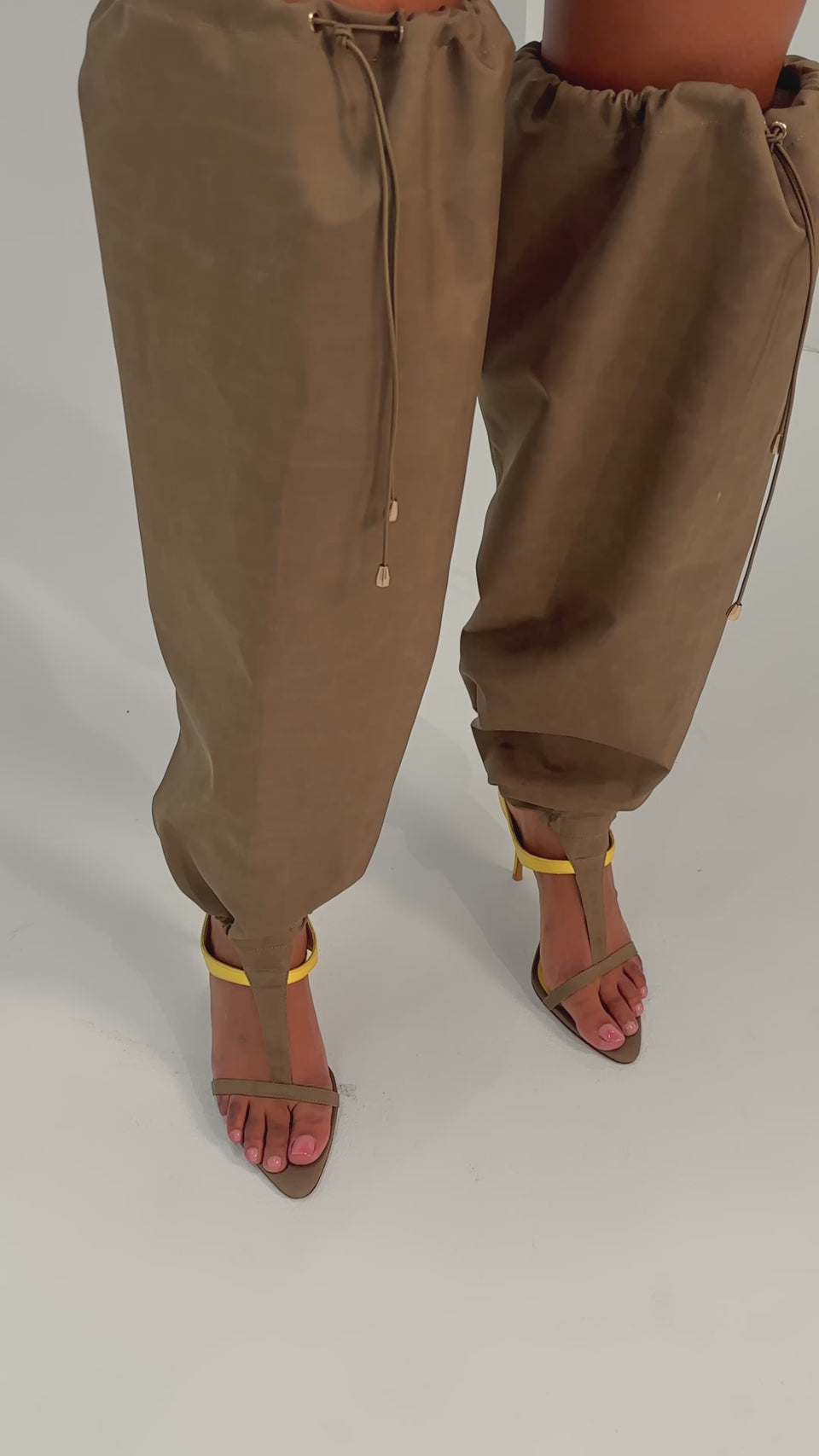 A video of a person wearing the AKIRA GOLD ZIDANE OLIVE CANVAS SLOUCHY STILETTO SANDALS for a bold, streetwear-inspired look on a plain background.