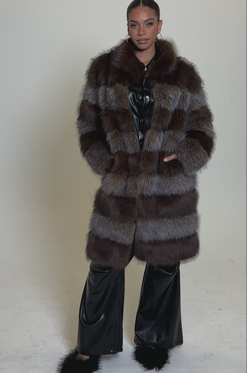 A video of a woman wearing the LITTLE BIT OF SPICE PANELED FAUX FUR COAT in brown and gray stripes over black leather pants and a black leather shirt, paired with fluffy black shoes.