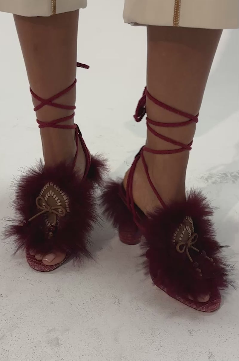 Video of a woman modeling the AKIRA GOLD UMIKA BURGUNDY FUR BLOCK SANDAL—boho-chic festival shoes with lace-up styling, embellished with faux fur and decorative details.