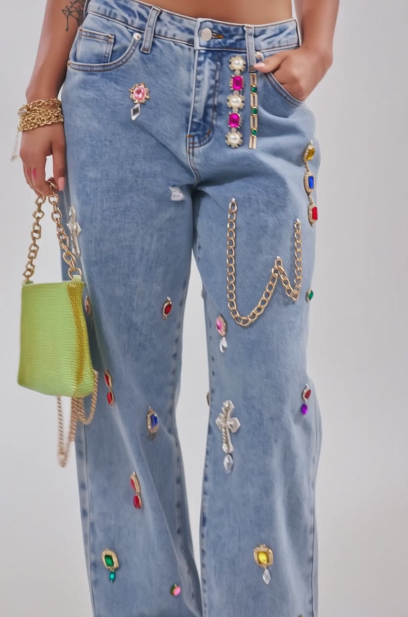 Video of woman modeling the FEELING THE DIFFERENCE EMBELLISHED RELAXED DENIM jeans with colorful rhinestones and gold chains, paired with a yellow sparkly handbag and gold sandals.