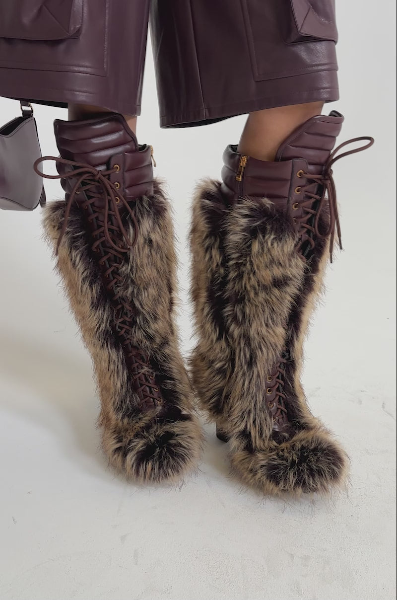 A video of a person in a burgundy faux leather outfit wearing the AZALEA WANG HEARTBEAT BROWN MULTI BLOCK FUR BOOT.