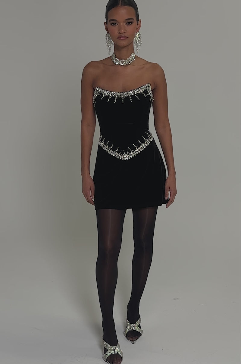 Video of woman modeling the HIGH SOCIETY VELVET RHINESTONE MINI DRESS, featuring a strapless design with sparkling silver embellishments, paired with statement earrings and a matching choker.