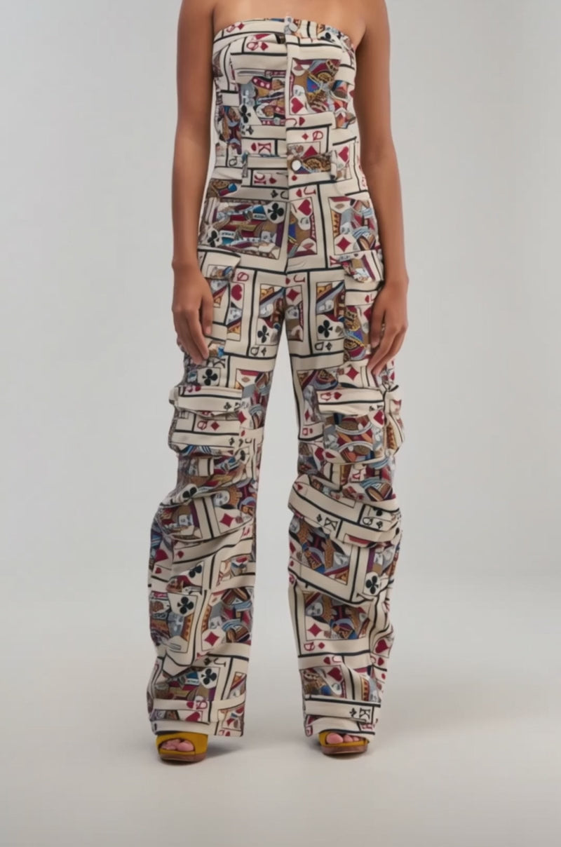 Video of a woman modeling the NO ONE LIKE ME Card Print Cargo Jumpsuit, featuring a colorful patchwork design and wide-leg pants.
