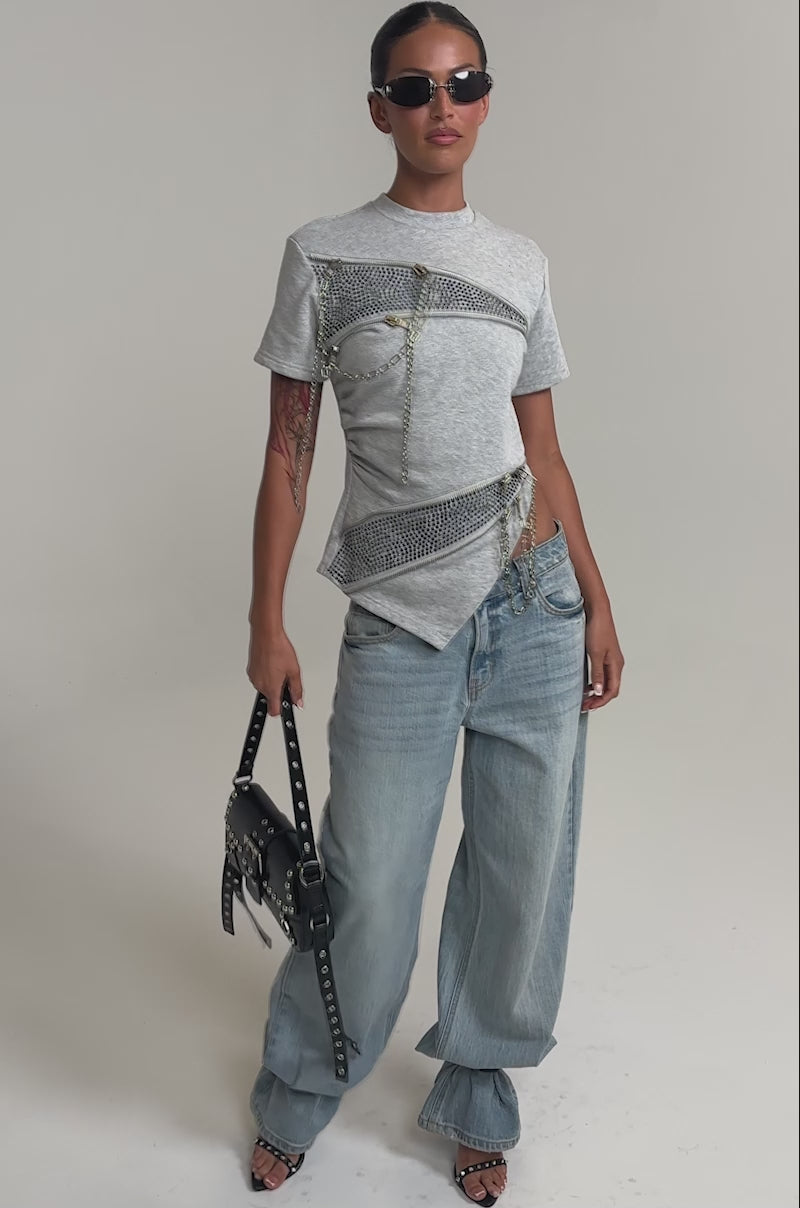 Video of woman modeling the DONT MESS OVERSIZED SWEATSHIRT, sunglasses, and light blue jeans, standing with one hand in their pocket against a plain background.
