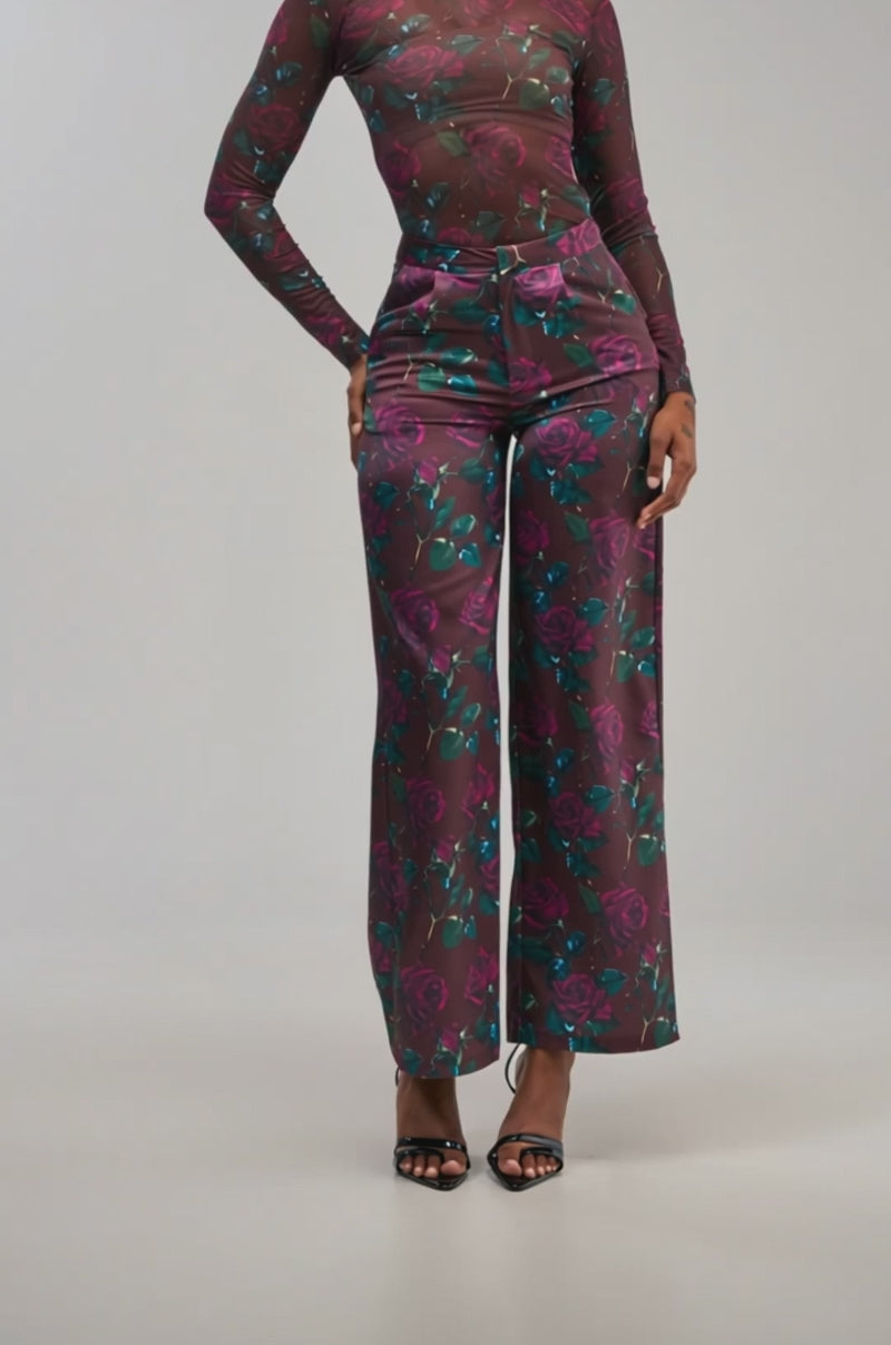 Video of a woman modeling the DOZEN ROSES SATIN PANT IN BURGUNDY with a wide-leg silhouette and matching sheer, long-sleeve floral print top.
