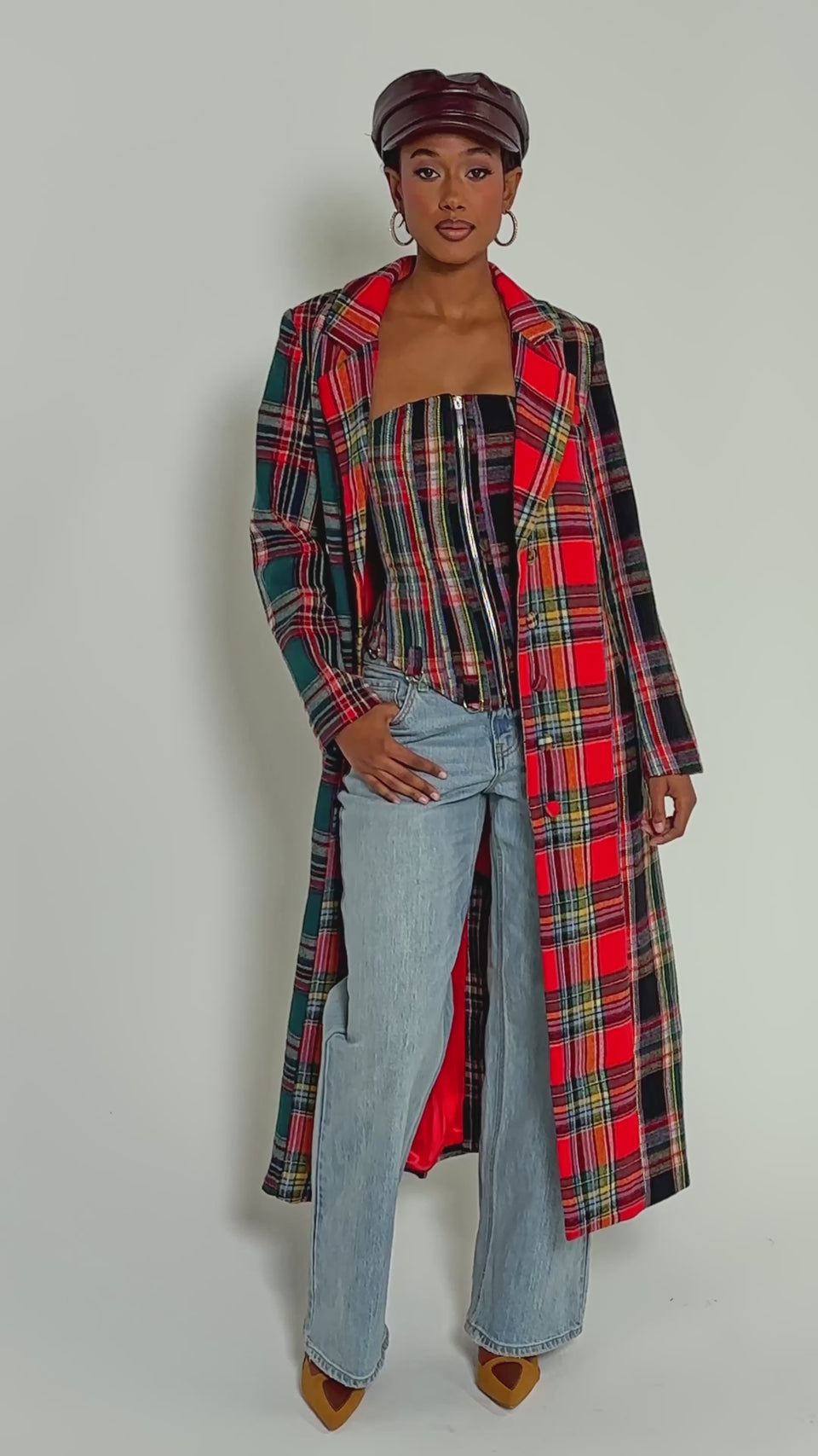 Video of woman modeling the TALK TO ME NICE PATCHWORK TRENCH over a matching top and light blue jeans, accessorized with a brown dog-shaped bag, dark leather cap, and hoop earrings.