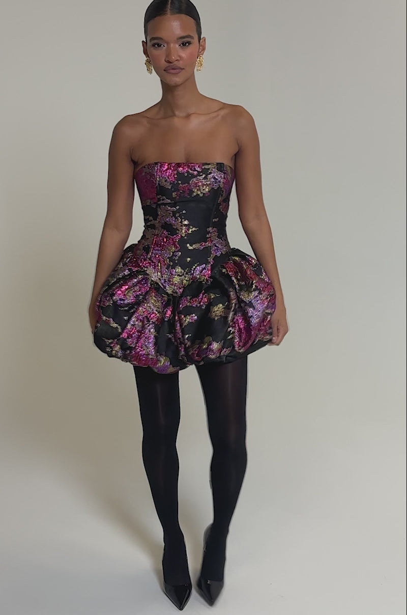 Video of woman modeling the SHOW STOPPER BROCADE MINI DRESS IN PURPLE, a strapless bubble skirt dress with pink and gold floral brocade, accessorized with gold statement earrings against a plain gray background.