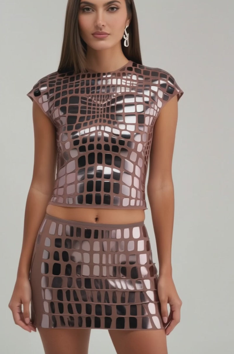 A video of a woman wearing the SEE THROUGH ME TOP, a shiny mirrored grid-patterned two-piece with metallic details and a matching mini skirt.