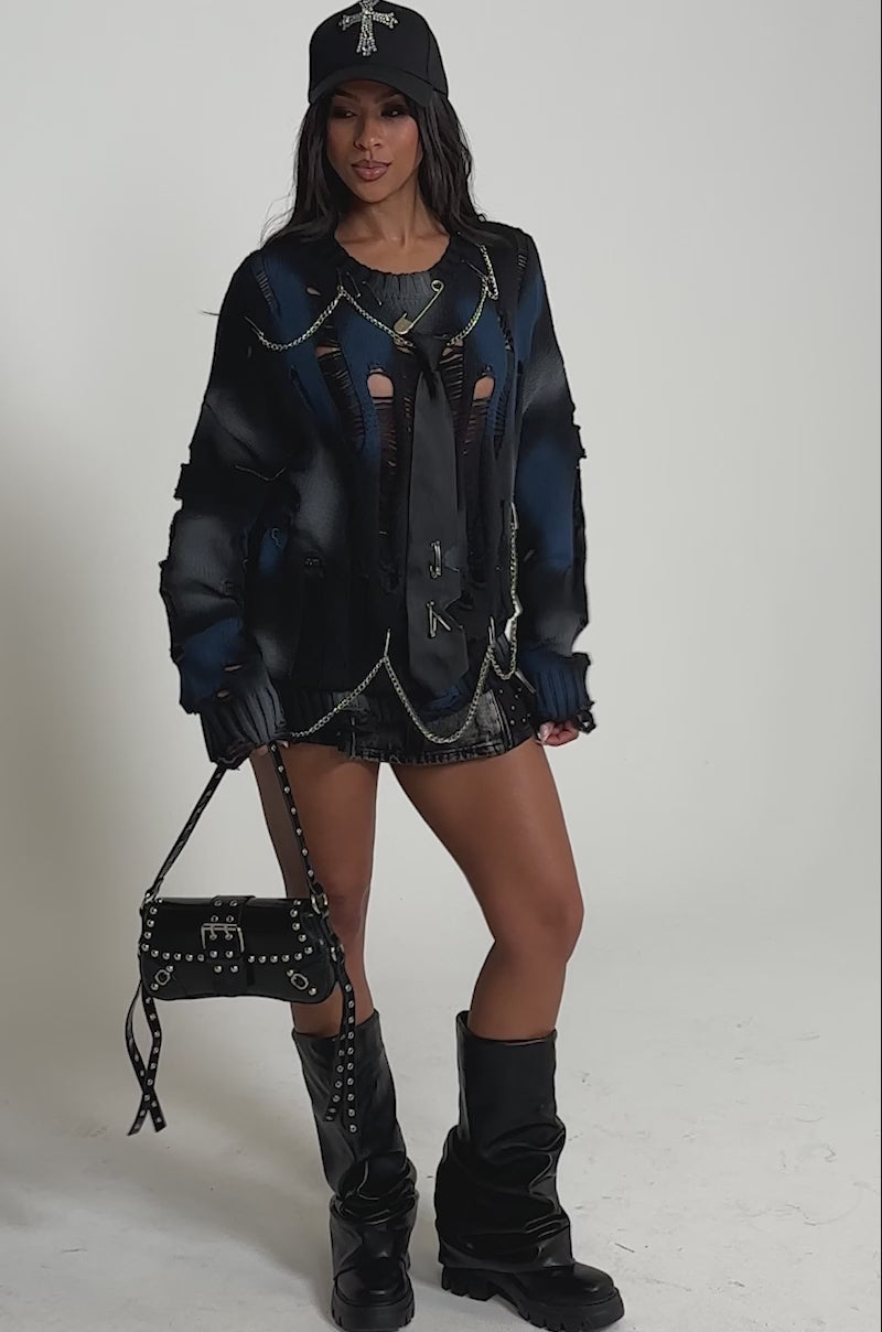 Video of woman modeling the RAWR DISTRESSED OVERSIZED SWEATER styled with a black cap, silver chains, a black tie, and a short black skirt.