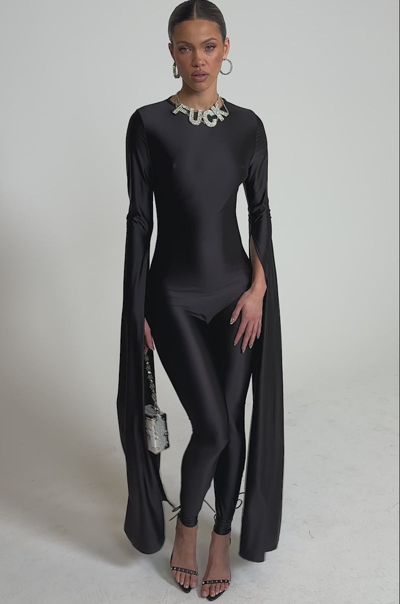 A video of a woman in the CATWALK QUEEN JUMPSUIT, featuring dramatic cape-like sleeve panels. 